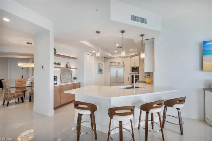 Kitchen breakfast bar, modern cabinets, a peninsula, appliances with stainless steel finishes, and floating shelves with custom lighting