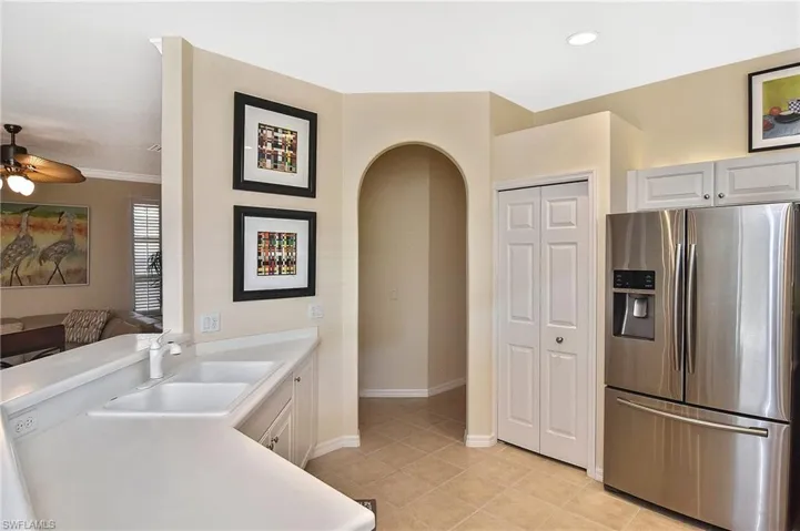 Kitchen featuring stainless steel fridge, light countertops, arched walkways, light tile patterned floors, and ceiling fan
