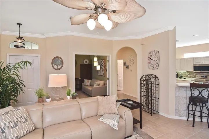 Living area with crown molding, light tile patterned flooring, arched walkways, and a ceiling fan