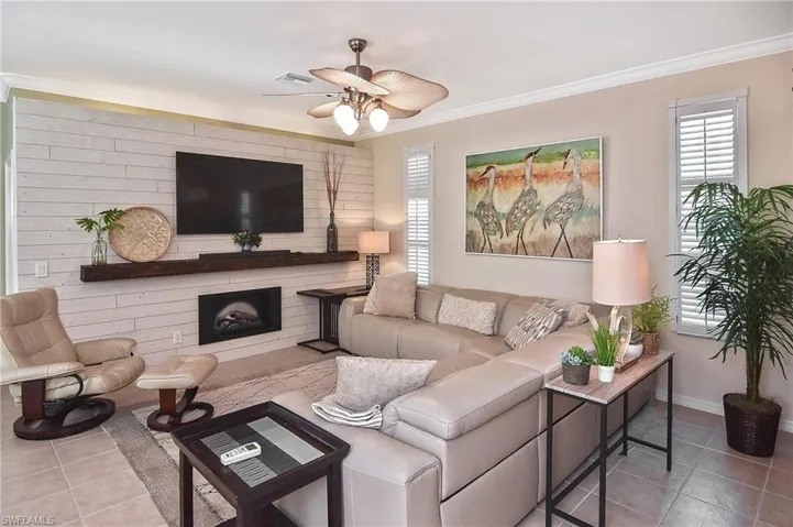 Living room featuring light tile patterned flooring, ornamental molding, a large fireplace, and ceiling fan