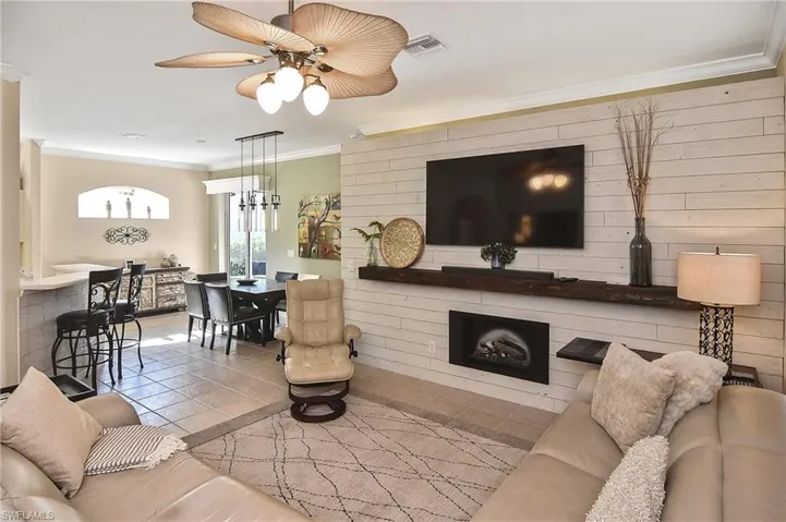 Tiled living room featuring ornamental molding, a fireplace, and a ceiling fan