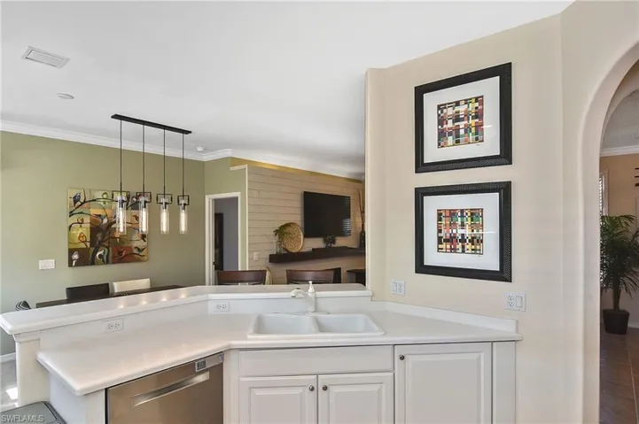 Kitchen featuring pendant lighting, a peninsula, stainless steel dishwasher, white cabinetry, and light countertops