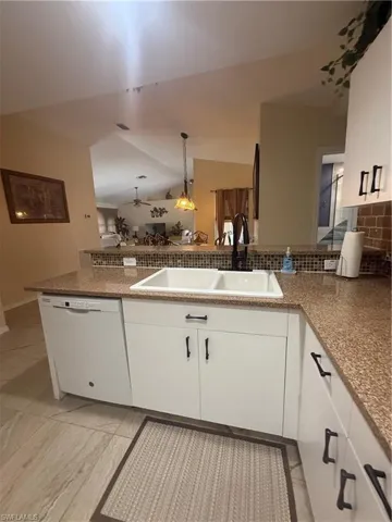 Kitchen with dishwashing machine, lofted ceiling, decorative backsplash, white cabinets, and hanging light fixtures