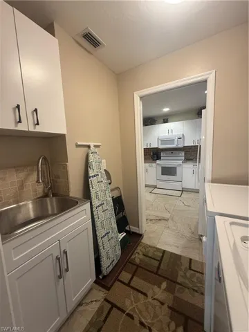 Kitchen featuring stove, washer and dryer, light marble finish floors, decorative backsplash, and white cabinetry