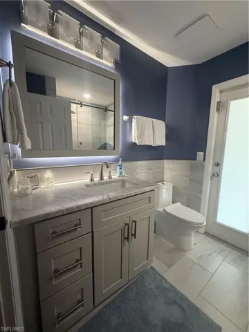 Full bath with vanity, marble finish floors, a wainscoted wall, and a shower