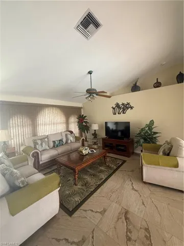 Living area with a ceiling fan, plenty of natural light, lofted ceiling, and marble look tile flooring