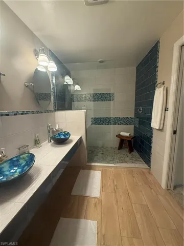 Bathroom featuring tile walls, wood finished floors, walk in shower, and vanity