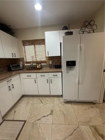 Kitchen with refrigerator, decorative backsplash, white cabinetry, dark countertops, and light marble finish floors