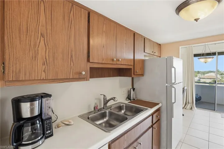 Kitchen with light countertops, freestanding refrigerator, light tile patterned flooring, and brown cabinets