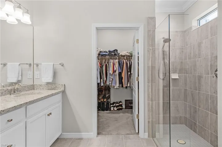 Full bath with crown molding, a spacious closet, vanity, and a tile shower