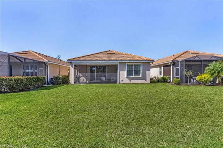 Rear view of house with a yard, a sunroom, stucco siding, and a tile roof