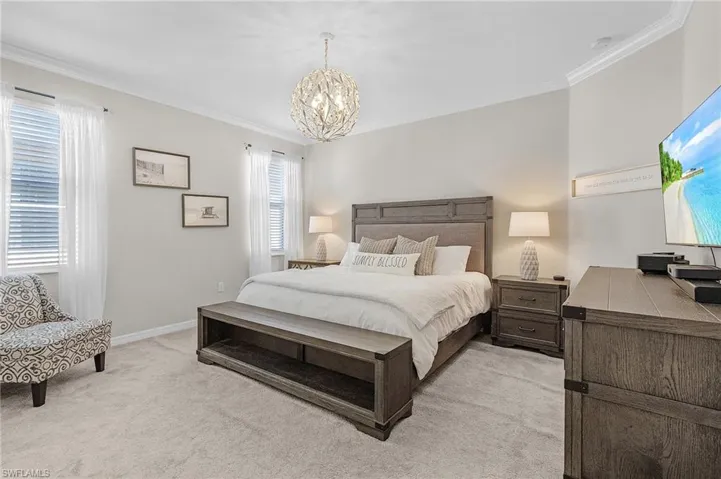 Bedroom featuring a chandelier, light colored carpet, crown molding, and baseboards