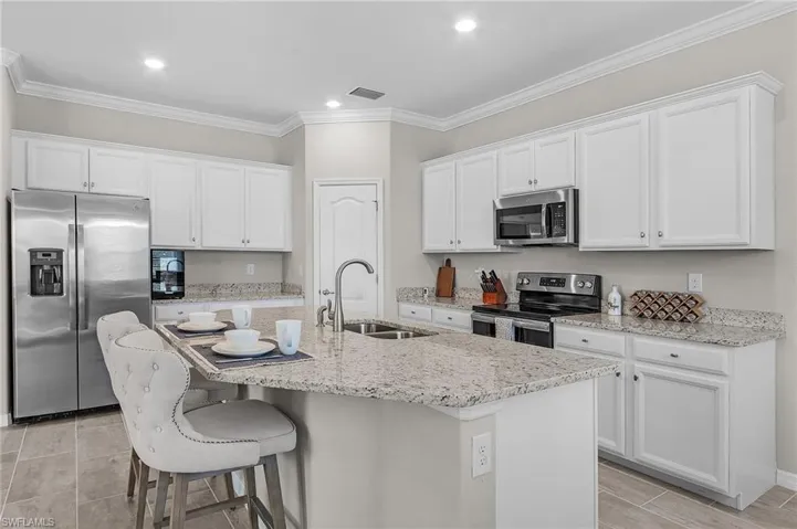 Kitchen featuring visible vents, an island with sink, a sink, stainless steel appliances, and white cabinets