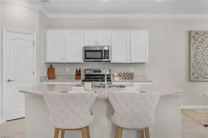 Kitchen featuring light stone counters, an island with sink, white cabinets, appliances with stainless steel finishes, and crown molding
