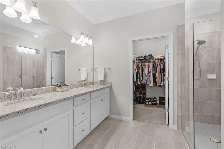 Bathroom with double vanity, a shower stall, crown molding, and a sink