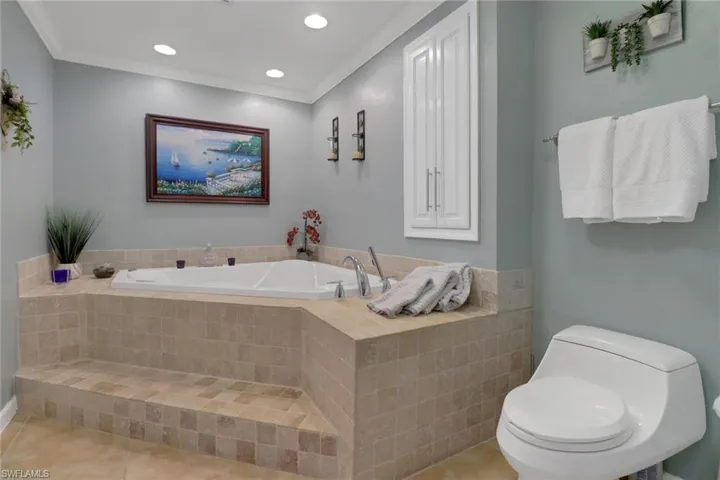 Bathroom with toilet, tile patterned flooring, tiled bath, and ornamental molding