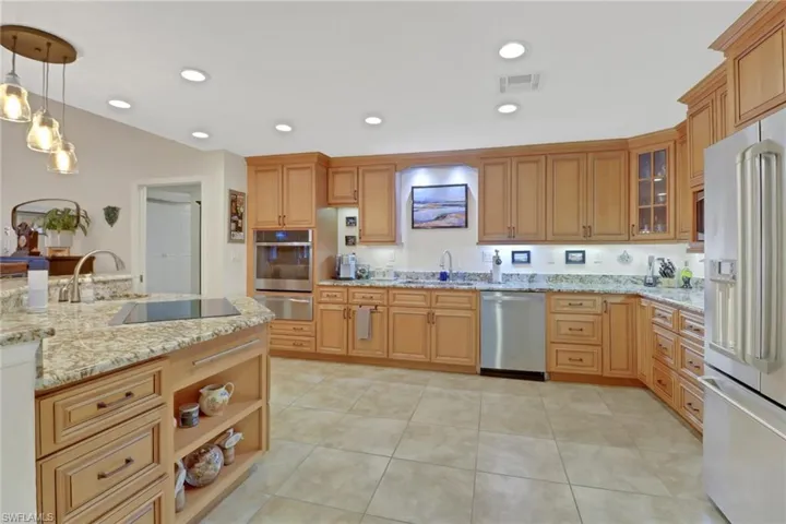 Kitchen with light stone countertops, appliances with stainless steel finishes, decorative light fixtures, sink, and light tile patterned floors