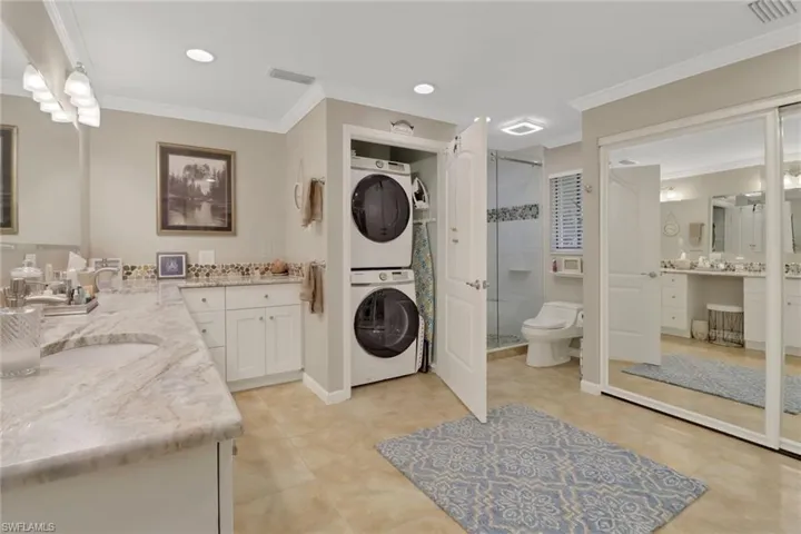 Bathroom with stacked washer / dryer, vanity, toilet, walk in shower, and ornamental molding