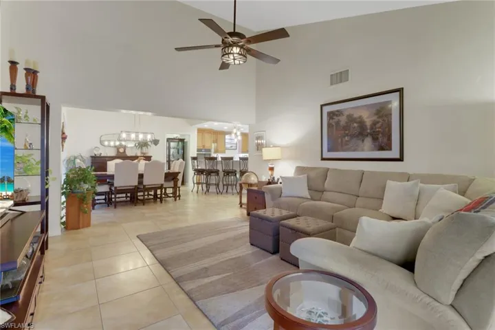 Living room with high vaulted ceiling, light tile patterned floors, and ceiling fan with notable chandelier