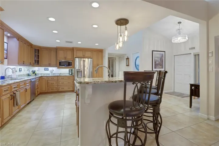 Kitchen with appliances with stainless steel finishes, decorative light fixtures, an inviting chandelier, sink, and a center island with sink