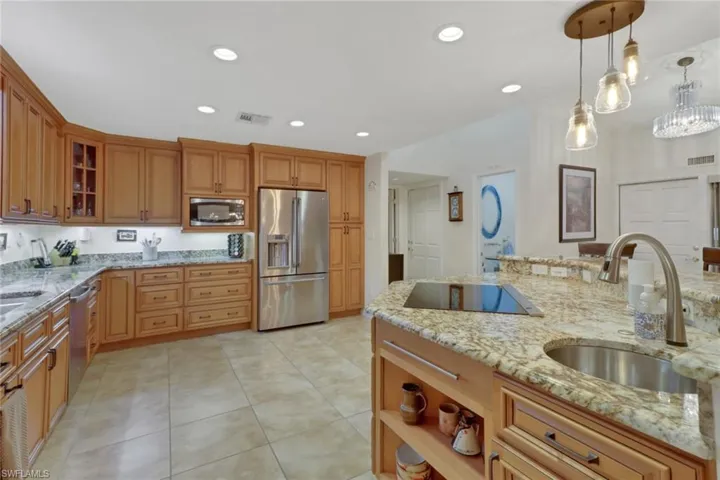 Kitchen with sink, hanging light fixtures, light stone countertops, appliances with stainless steel finishes, and light tile patterned floors