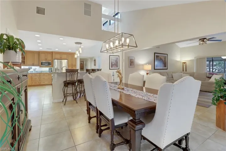 Dining room featuring light tile patterned floors, ceiling fan with notable chandelier, and a high ceiling
