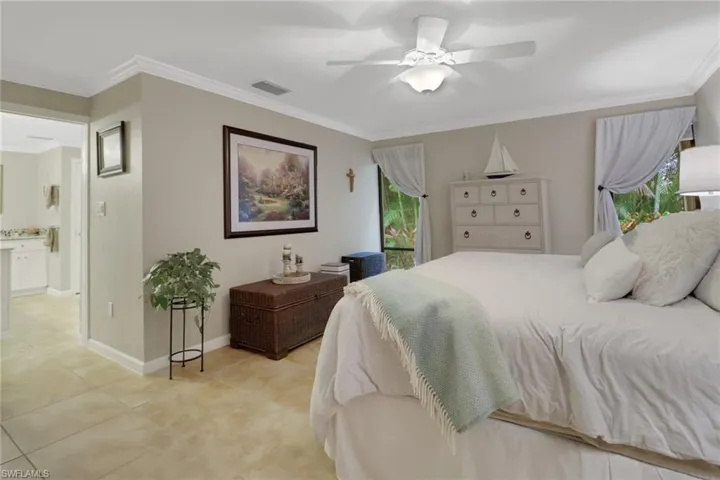 Tiled bedroom featuring ceiling fan, crown molding, and connected bathroom