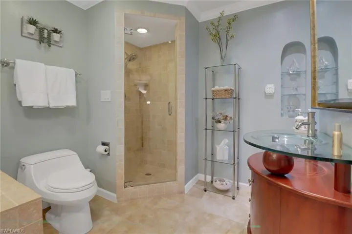 Bathroom featuring toilet, a shower with door, tile patterned floors, ornamental molding, and sink