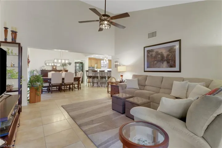 Living room featuring light tile patterned floors, ceiling fan with notable chandelier, and high vaulted ceiling