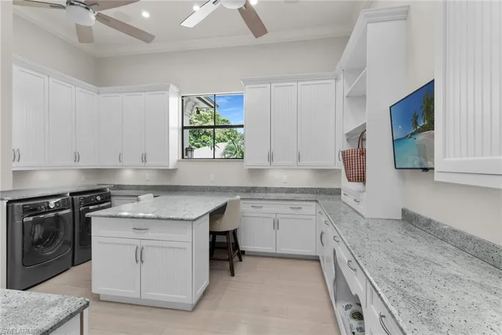 Spacious laundry room featuring extensive white cabinetry, light-toned countertops, an integrated island, and wood-finish flooring