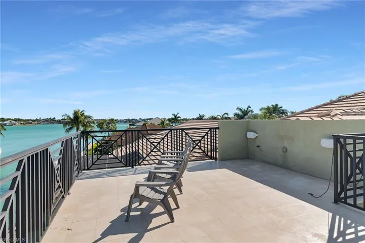 Expansive rooftop patio featuring a large tile surface, decorative metal railings, and broad water scenery