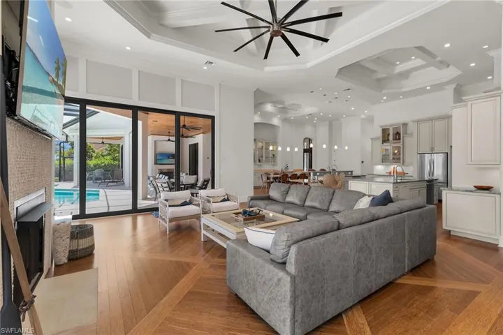 Spacious living area featuring coffered ceilings, wood-finish flooring with a distinctive pattern, and expansive sliding glass doors