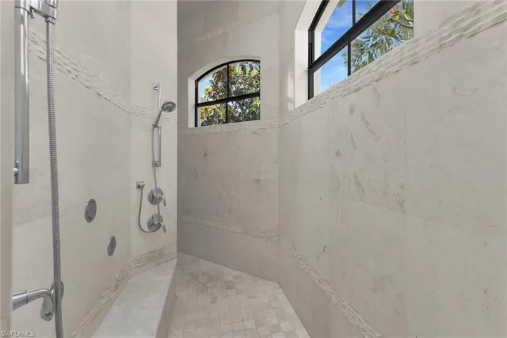 Spacious shower with large format wall tiles, a built-in bench, and multiple shower heads