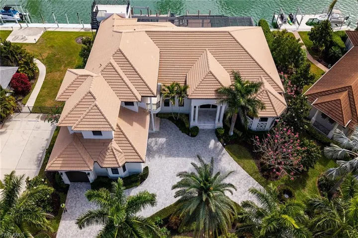 Waterfront residence featuring a terracotta-tiled roof, mature palm trees, a circular driveway, and a private dock