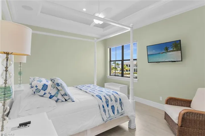 Recessed ceiling with an integrated ceiling fan and speaker, transom window, wall-mounted television, and light wood-finish flooring