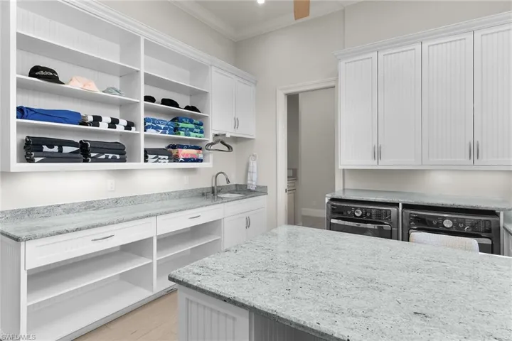Spacious laundry area featuring extensive white cabinetry, granite countertops, an undermount sink, and a large central island
