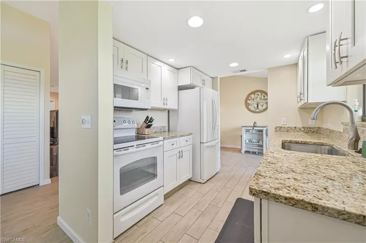 Kitchen with white appliances, light stone counters, white cabinetry, wood tiled floors, and recessed lighting