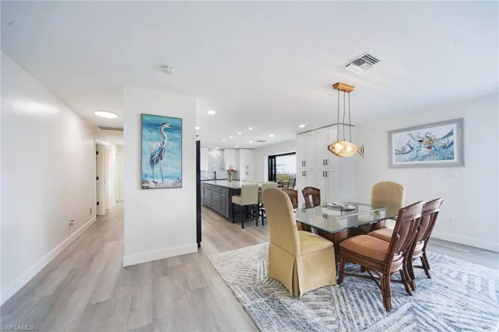 Dining Area and kitchen island. Hallway to left leads to primary suite and one of two guest bedrooms.