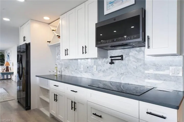 Perimeter counters are Silestone Quartz in Charcoal Soapstone Suede. Features glass cooktop, microwave, wall mounted pot filler, white wood cabinetry and pull out drwaers.