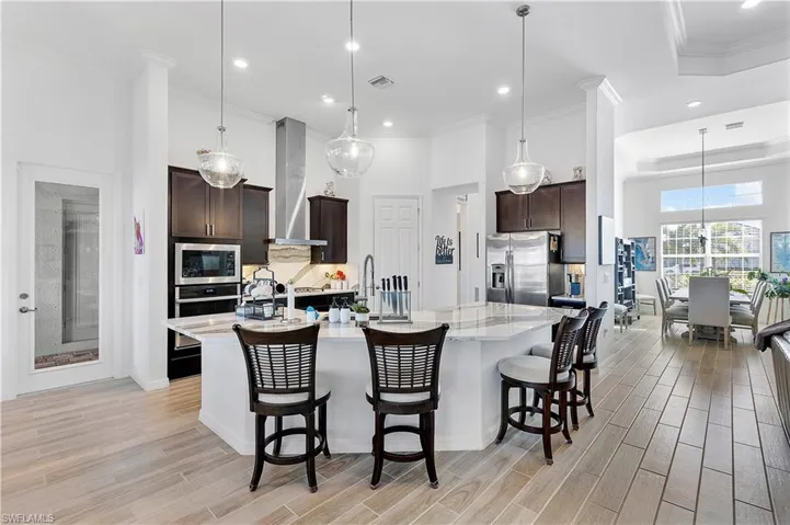 Kitchen featuring tasteful backsplash, stainless steel appliances, dark brown cabinetry, wall chimney range hood, and wood tiled floor