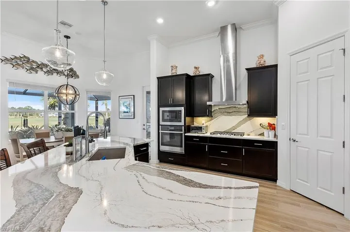 Kitchen featuring a sink, appliances with stainless steel finishes, crown molding, and wall chimney range hood