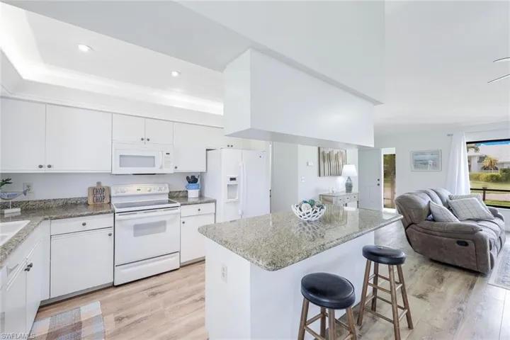 Kitchen featuring a tray ceiling, white cabinets, white appliances, light hardwood / wood-style flooring, and a kitchen breakfast bar