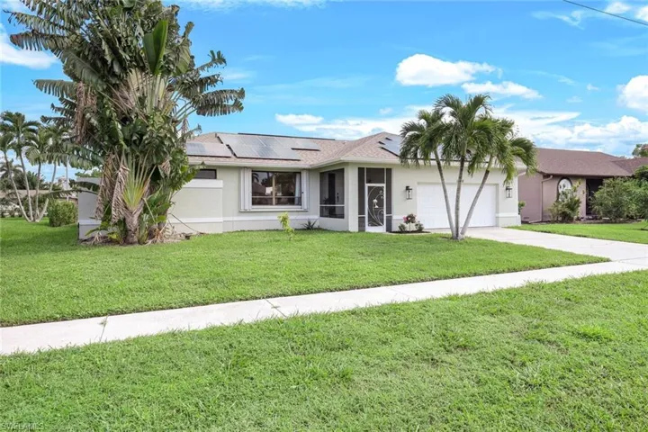 Single story home featuring solar panels, a garage, and a front lawn
