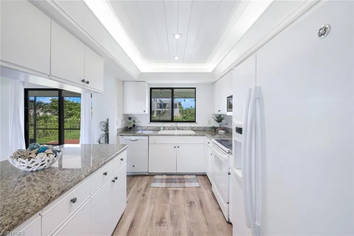 Kitchen featuring white cabinetry, light hardwood / wood-style flooring, white appliances, light stone countertops, and sink