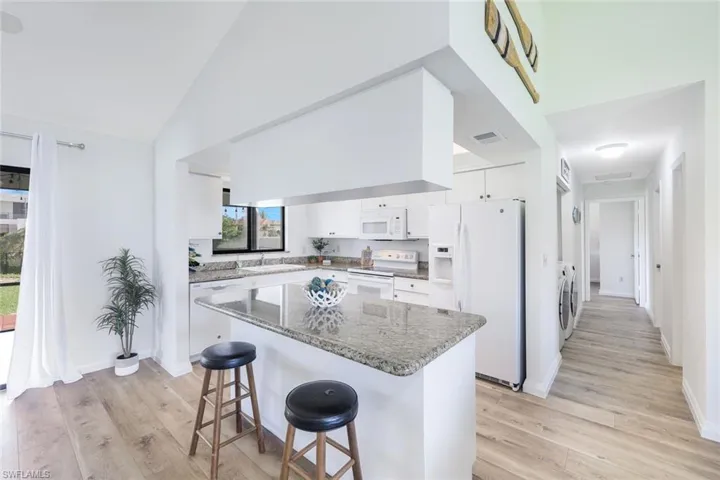 Kitchen featuring light hardwood / wood-style flooring, white appliances, white cabinets, a center island, and sink
