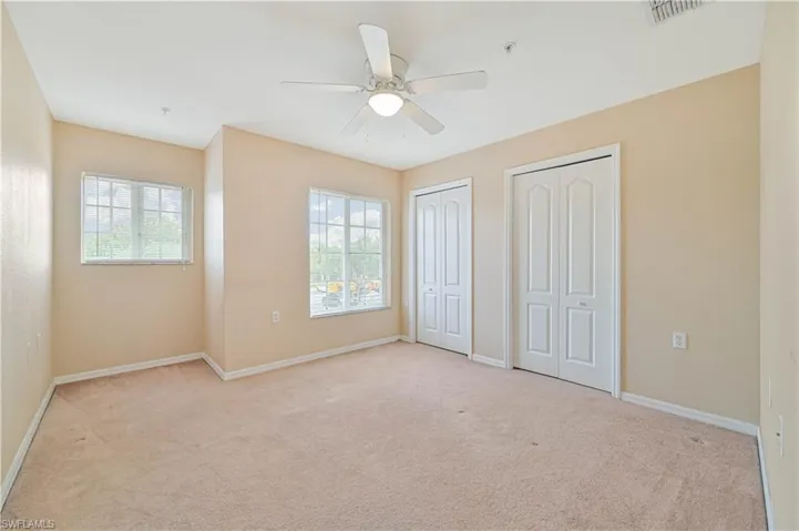 Unfurnished bedroom with light colored carpet, ceiling fan, multiple closets, and multiple windows