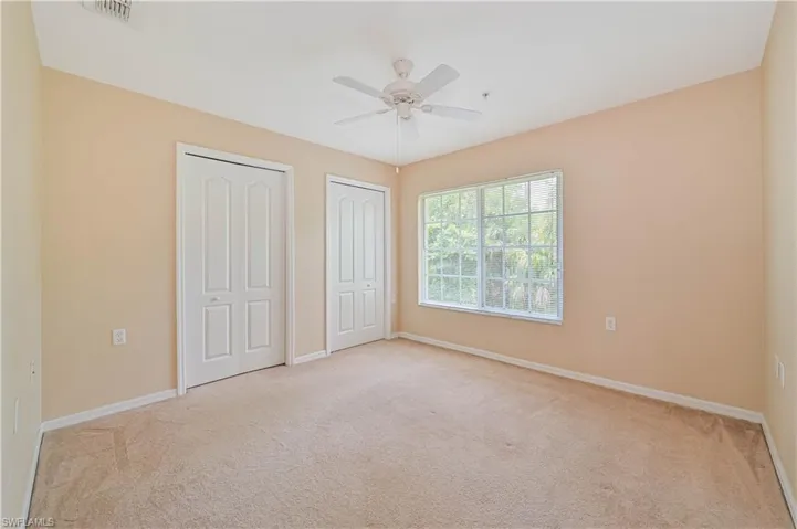 Unfurnished bedroom with light colored carpet, ceiling fan, and multiple closets