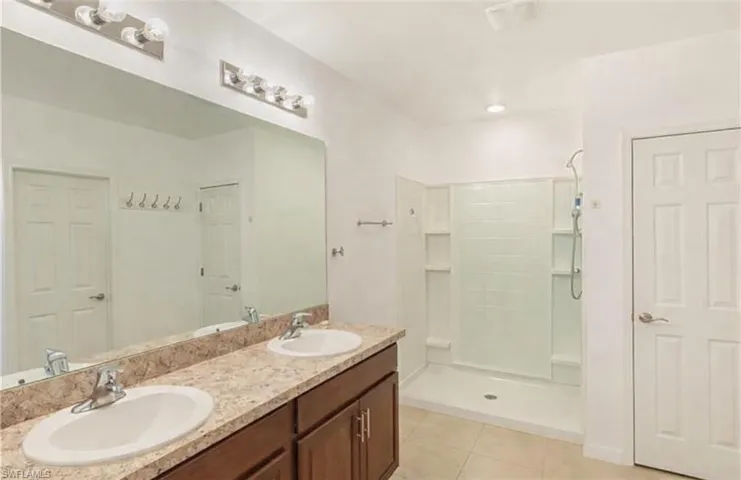 Full bathroom featuring double vanity, a shower stall, and light tile patterned floors