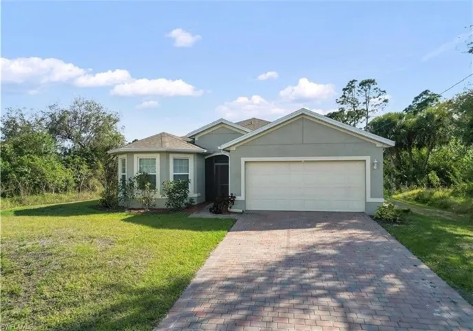 Ranch-style house featuring stucco siding, a front lawn, decorative driveway, and a garage