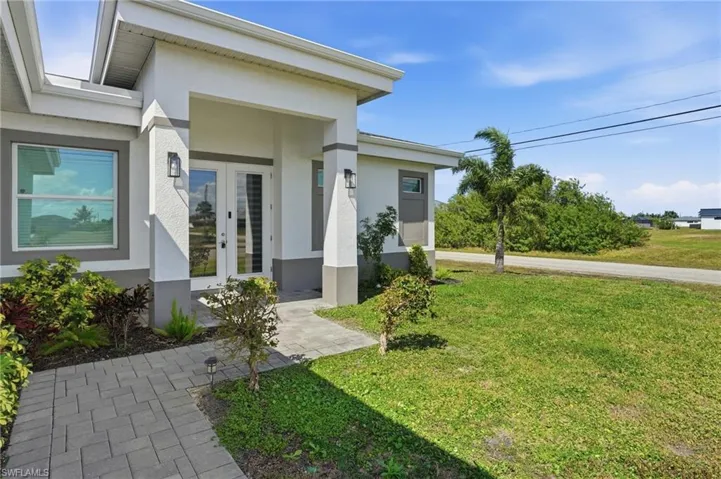 Entrance to property with french doors, a lawn, and stucco siding